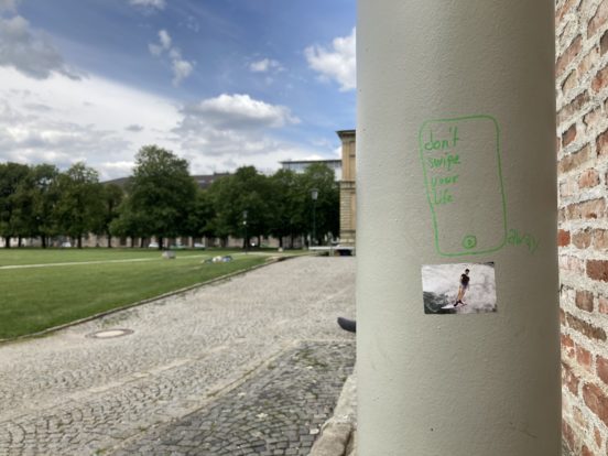Ein Plätzchen vor der alten Pinakothek in München. Auf einer Säule steht mit grünem Textmarker geschrieben: Don't swipe your life away.